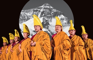 The Tashi Lhunpo monks in ceremonial orange robes and tall yellow hats, against a black-and-white photo of a giant mountain